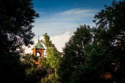 College Hall's bell tower poking out above some trees on a sunny day near dusk.